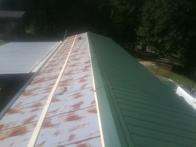 Old rusted panels beside newly installed green metal roofing — Wind Damage Roof Repair by Roofing Brothers in Vermillion
