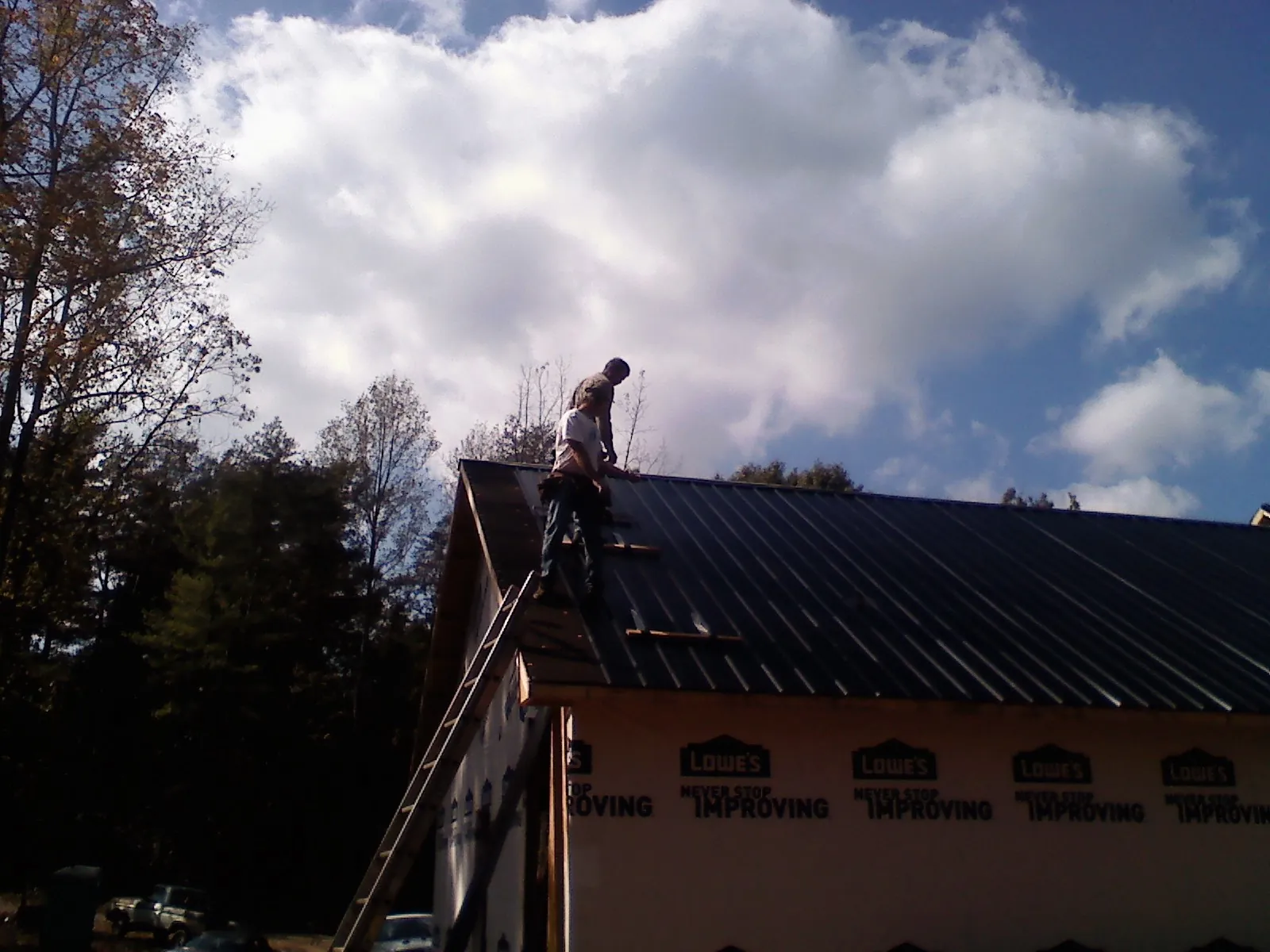 Roofer fastening dark metal panels high against a cloudy sky, from a Roof Inspection job in Vermillion